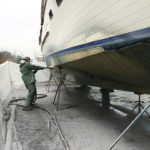 Man removing paint from the bottom of a boat as part of Central Alabama Mobile Sandblasting's marine sandblasting services